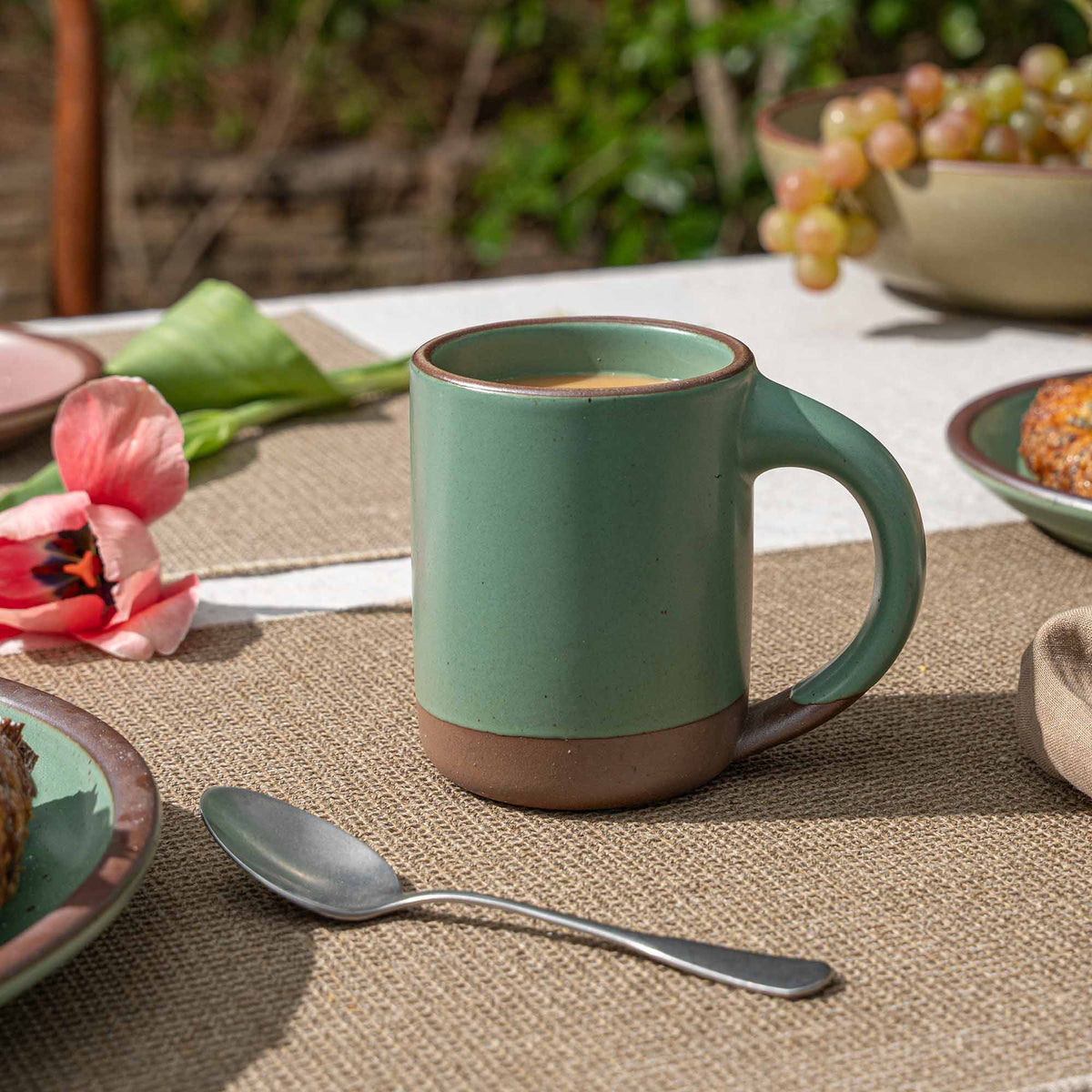 Ceramic mug with straight sides and handle, made from iron-rich speckled stoneware with a raw rim in a viridian green glaze with a matte finish.