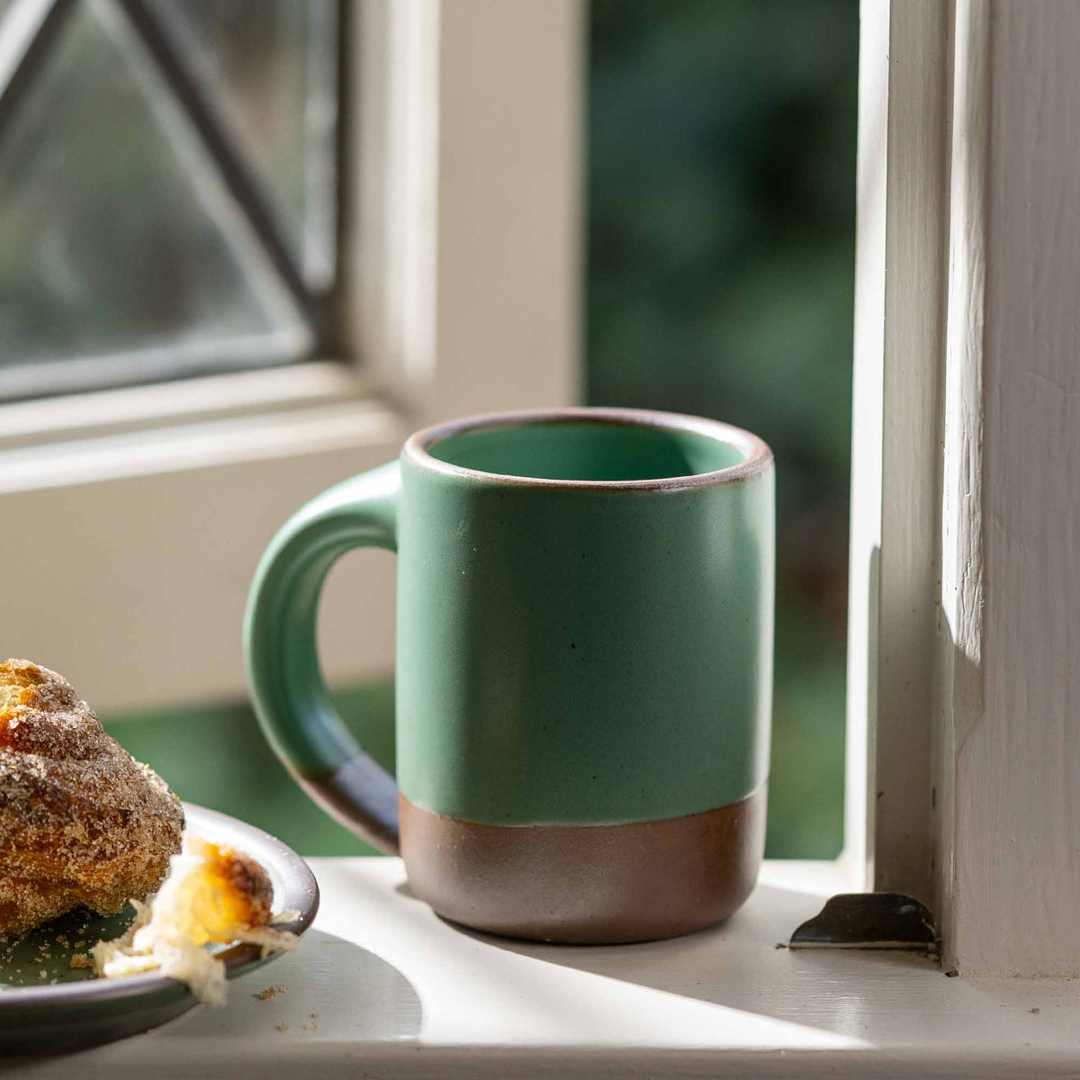 Ceramic mug with straight sides and handle, made from iron-rich speckled stoneware with a raw rim in a viridian green glaze with a matte finish.