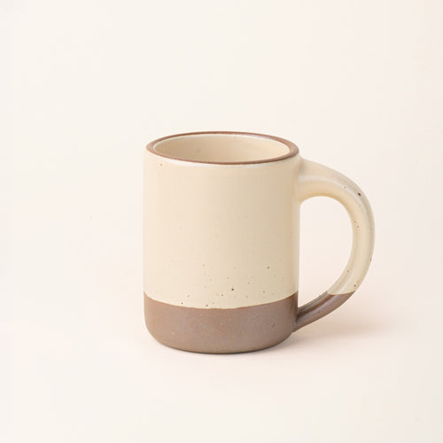 A big sized ceramic mug with handle in a cream color featuring iron speckles and unglazed rim and bottom base.