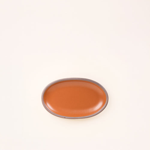 A small oval ceramic platter in an earthy orange color featuring iron speckles and an unglazed rim