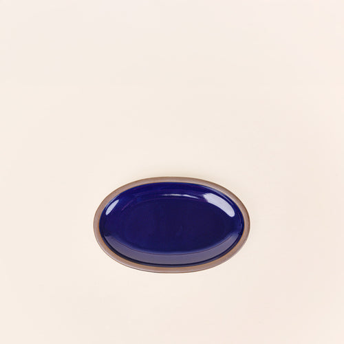 A small oval ceramic platter in a glossy dark blue color featuring iron speckles and an unglazed rim