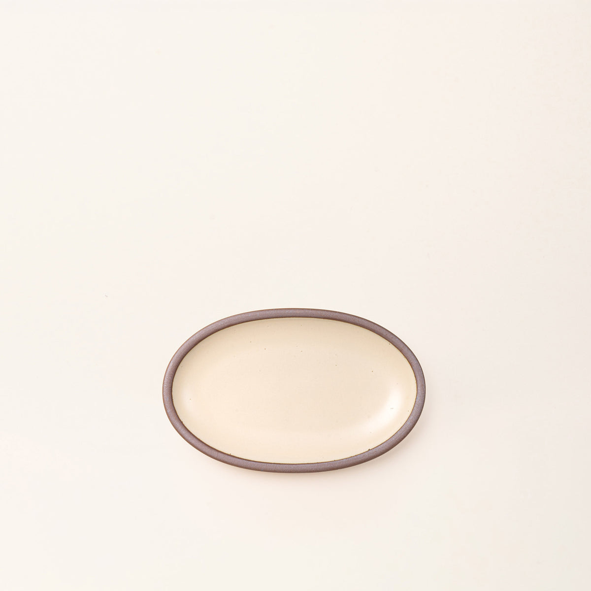 A small oval ceramic platter in a cream color featuring iron speckles and an unglazed rim