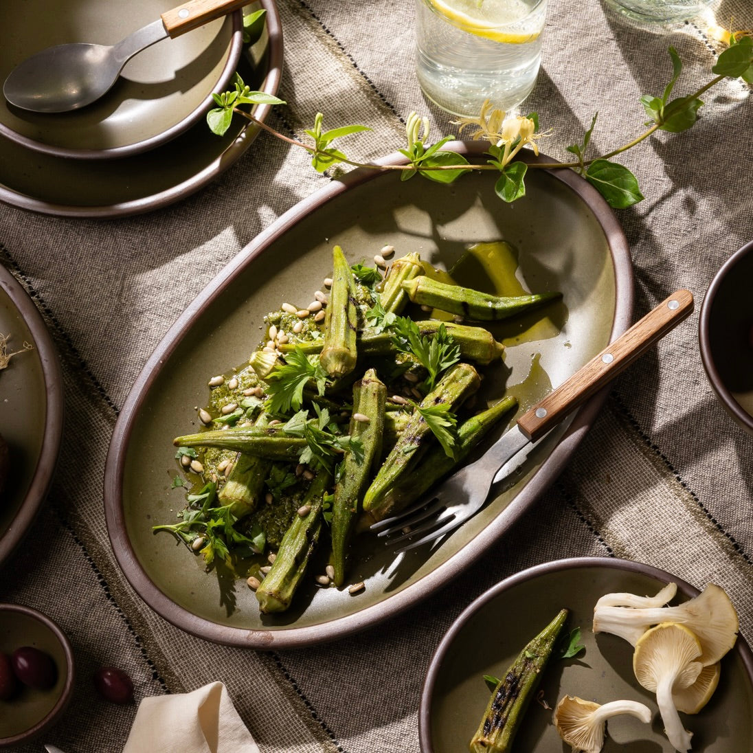 Olive-toned stoneware oval platter, styled with grilled okra and herbs on a rustic linen table.