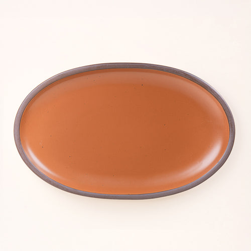 A large oval ceramic platter in an earthy orange color featuring iron speckles and an unglazed rim