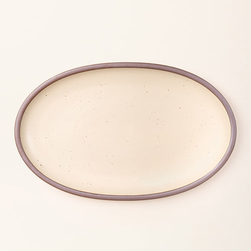 A large oval ceramic platter in a cream color featuring iron speckles and an unglazed rim