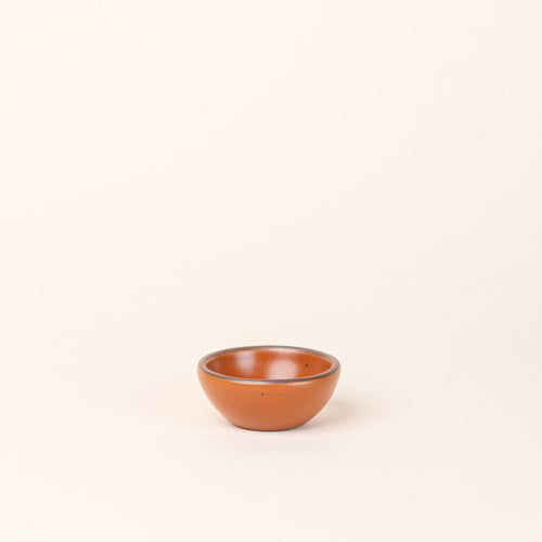 A tiny rounded ceramic bowl in an earthy orange color featuring iron speckles and an unglazed rim
