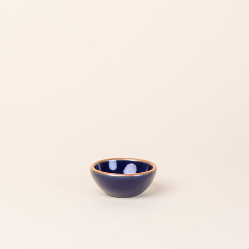 A tiny rounded ceramic bowl in a glossy dark blue color featuring iron speckles and an unglazed rim