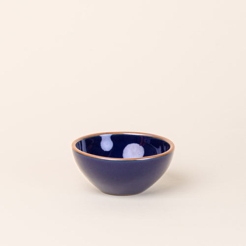 A small dessert sized rounded ceramic bowl in a glossy dark blue color featuring iron speckles and an unglazed rim