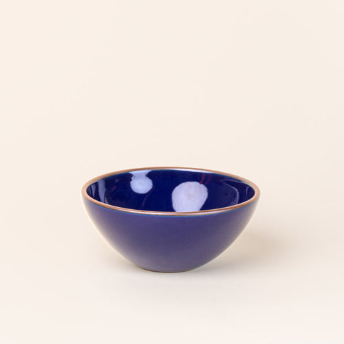 A medium rounded ceramic bowl in a glossy dark blue color featuring iron speckles and an unglazed rim