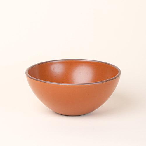 A large rounded ceramic bowl in an earthy orange color featuring iron speckles and an unglazed rim