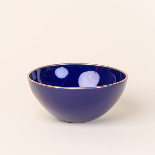 A large rounded ceramic bowl in a glossy dark blue color featuring iron speckles and an unglazed rim