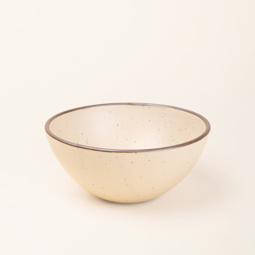 A large rounded ceramic bowl in a cream color featuring iron speckles and an unglazed rim