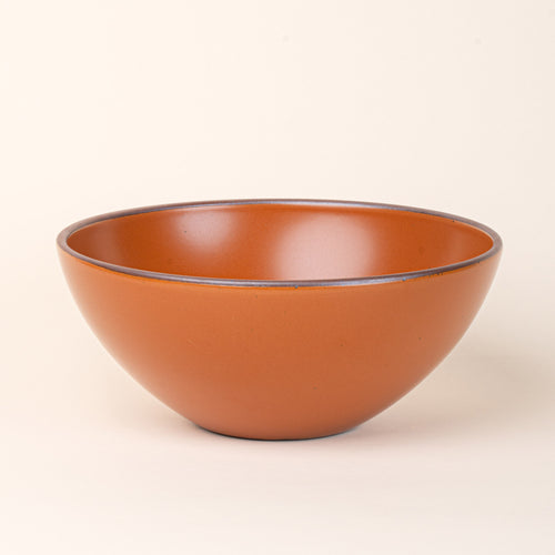 A large ceramic mixing bowl in an earthy orange color featuring iron speckles and an unglazed rim
