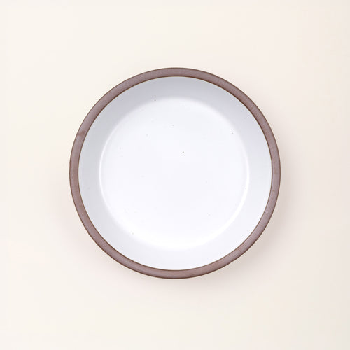 An overhead view of a shallow round ceramic pie plate in a cool white color featuring an unglazed rim, against a cream background.