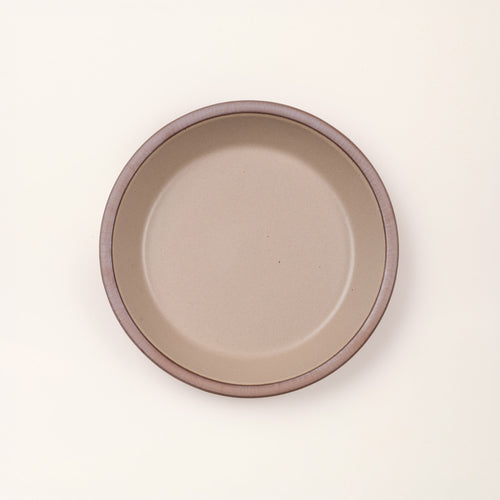 An overhead view of a shallow round ceramic pie plate in a pale warm brown color featuring an unglazed rim, against a cream background.