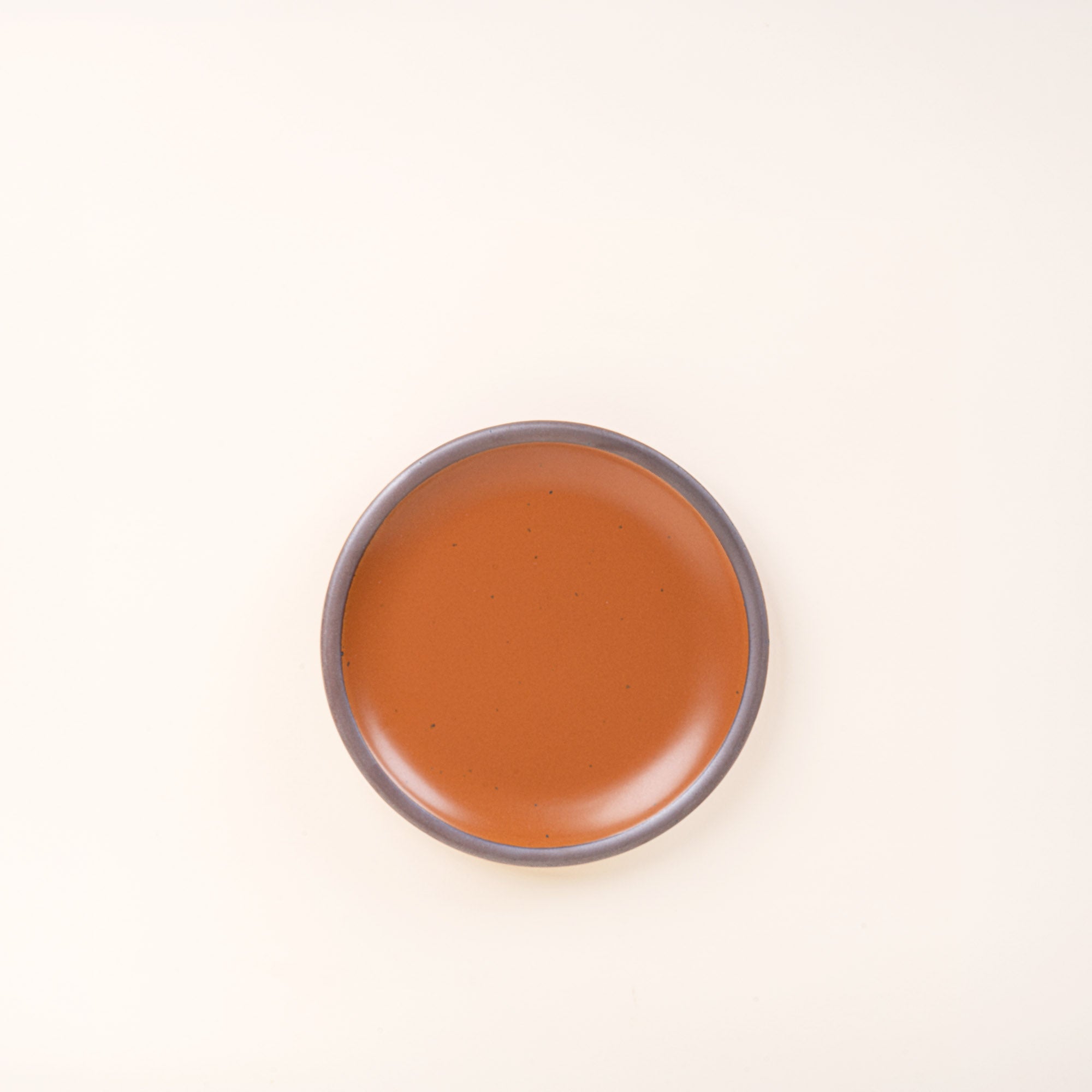 A dessert sized ceramic plate in an earthy orange color featuring iron speckles and an unglazed rim.