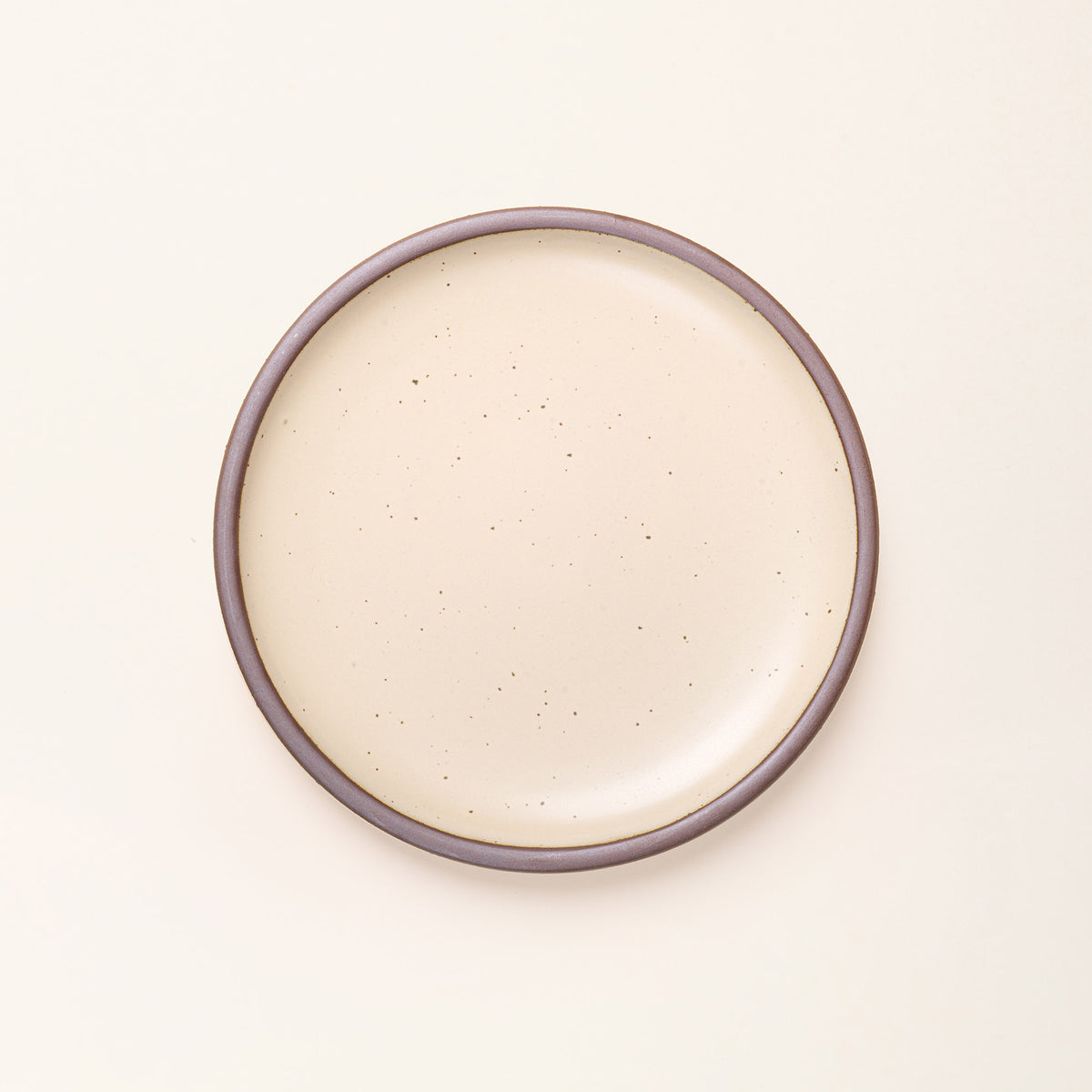 A dinner sized ceramic plate in a cream color featuring iron speckles and an unglazed rim