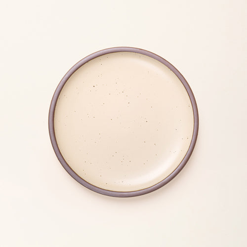 A dinner sized ceramic plate in a cream color featuring iron speckles and an unglazed rim