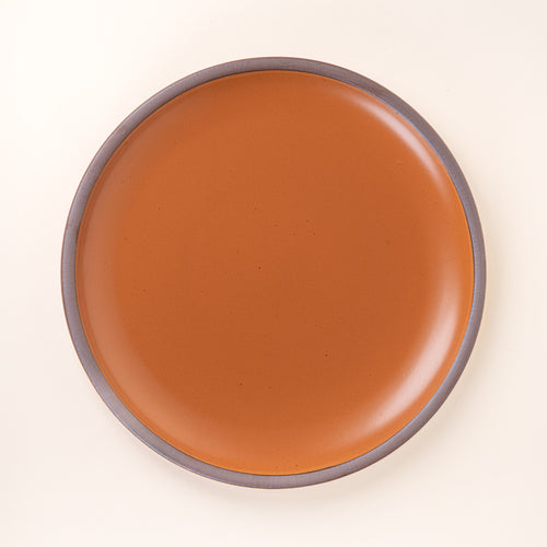 A large ceramic platter in an earthy orange color featuring iron speckles and an unglazed rim.