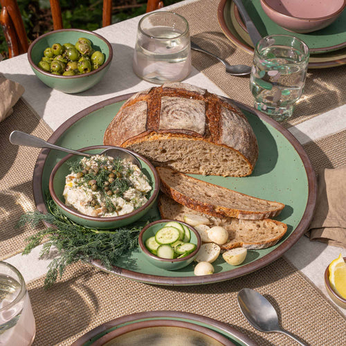 A wide ceramic platter for presenting dishes in a viridian green glaze with a matte finish.