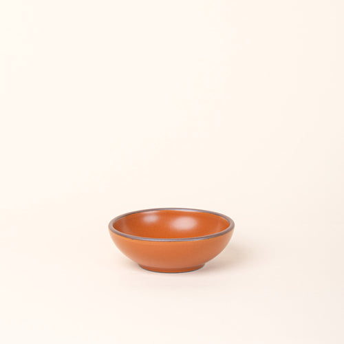 A small shallow ceramic bowl in an earthy orange color featuring iron speckles and an unglazed rim