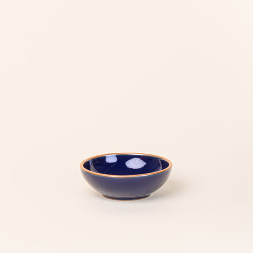 A small shallow ceramic bowl in a glossy dark blue color featuring iron speckles and an unglazed rim
