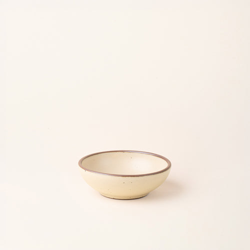 A small shallow ceramic bowl in a cream color featuring iron speckles and an unglazed rim