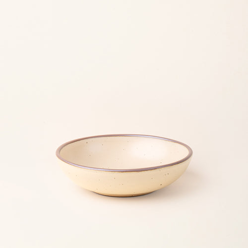 A dinner-sized shallow ceramic bowl in a cream color featuring iron speckles and an unglazed rim