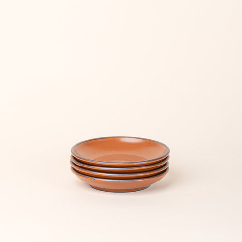 A stack of 4 small ceramic plates with a curved bowl edge in an earthy orange color featuring iron speckles and an unglazed rim.