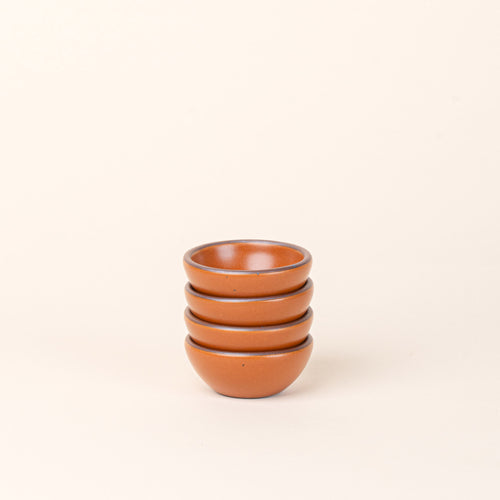 A stack of 4 tiny rounded ceramic bowls in an earthy orange color featuring iron speckles and an unglazed rim