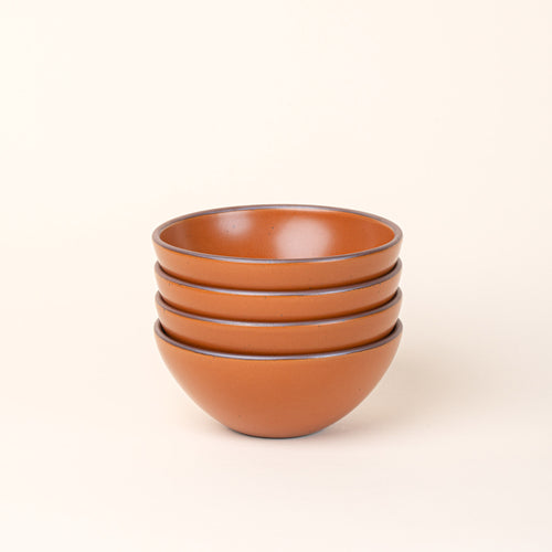 A stack of 4 medium rounded ceramic bowls in an earthy orange color featuring iron speckles and an unglazed rim