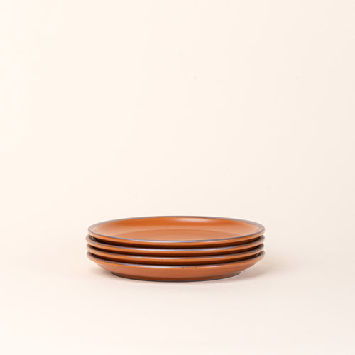 A stack of 4 medium sized ceramic plates in an earthy orange color featuring iron speckles and an unglazed rim.