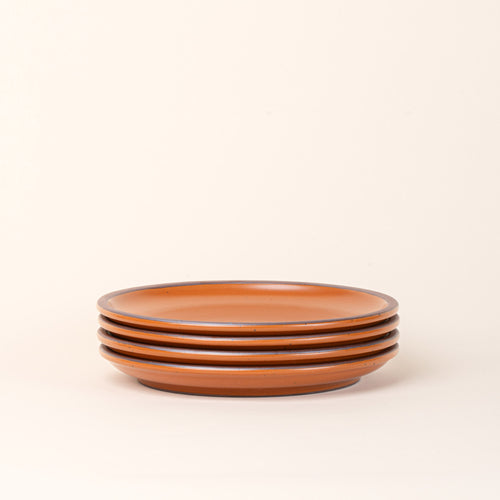 A stack of 4 dinner sized ceramic plates in an earthy orange color featuring iron speckles and an unglazed rim