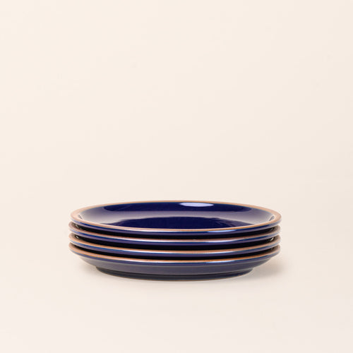 A stack of 4 dinner sized ceramic plates in a glossy dark blue color featuring iron speckles and an unglazed rim