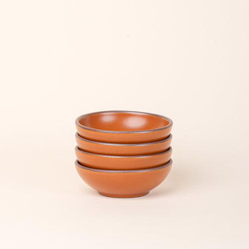 A stack of 4 small shallow ceramic bowls in an earthy orange color featuring iron speckles and an unglazed rim