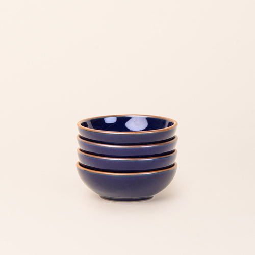 A stack of 4 small shallow ceramic bowls in a glossy dark blue color featuring iron speckles and an unglazed rim