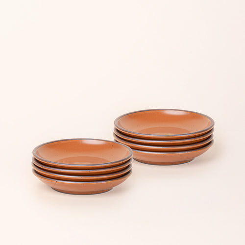 2 stacks of 4 small ceramic plates with a curved bowl edge in an earthy orange color featuring iron speckles and an unglazed rim.