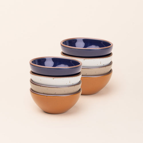 2 stacks of 4 small dessert sized rounded ceramic bowls in an earthy orange, glossy dark blue, white, and warm pale brown colors featuring iron speckles and an unglazed rim