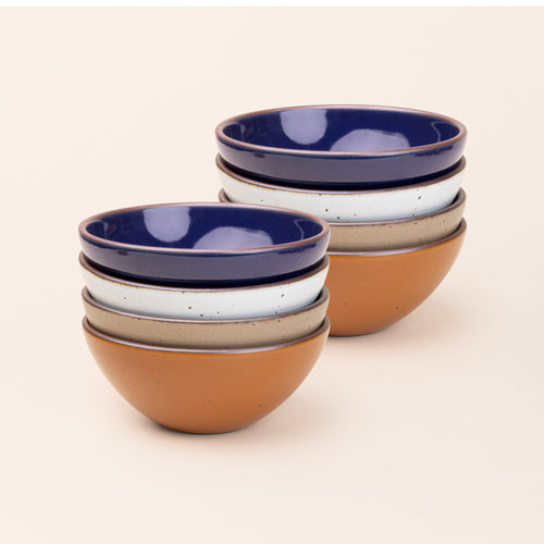 2 stacks of 4 medium sized rounded ceramic bowls in an earthy orange, glossy dark blue, white, and warm pale brown colors featuring iron speckles and an unglazed rim