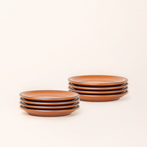 2 stacks of 4 dessert sized ceramic plates in an earthy orange color featuring an unglazed rim.