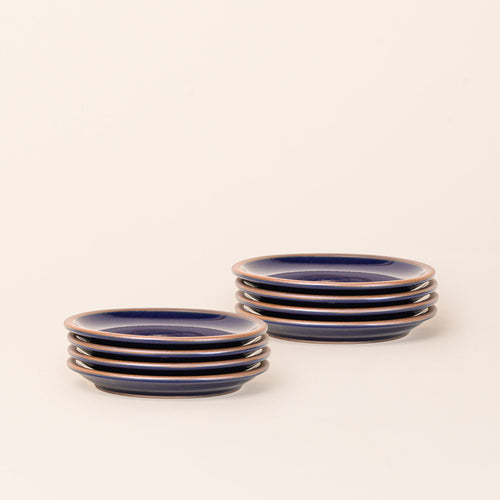 2 stacks of 4 dessert sized ceramic plates in a glossy dark blue color featuring an unglazed rim.