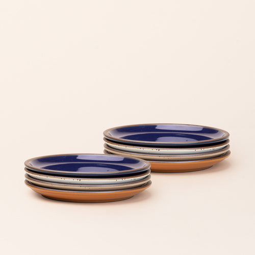 8 medium sized ceramic plates in a glossy dark blue, earthy orange, warm pale brown and white colors featuring iron speckles and an unglazed rim