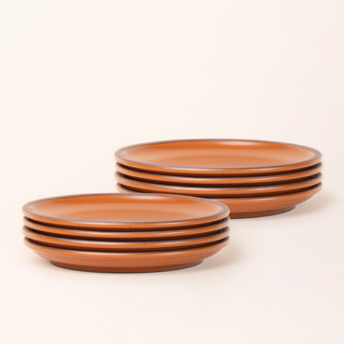 2 stacks of 4 dinner sized ceramic plates in an earthy orange color featuring iron speckles and an unglazed rim