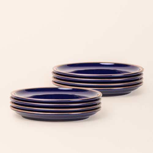 2 stacks of 4 dinner sized ceramic plates in a glossy dark blue color featuring iron speckles and an unglazed rim