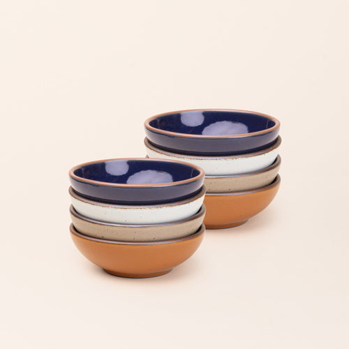 2 stacks of 4 small shallow ceramic bowls in an earthy orange, glossy dark blue, white, and warm pale brown colors featuring iron speckles and an unglazed rim
