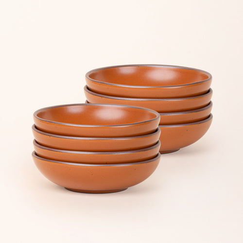 2 stacks of 4 dinner-sized shallow ceramic bowls in an earthy orange color featuring iron speckles and an unglazed rim