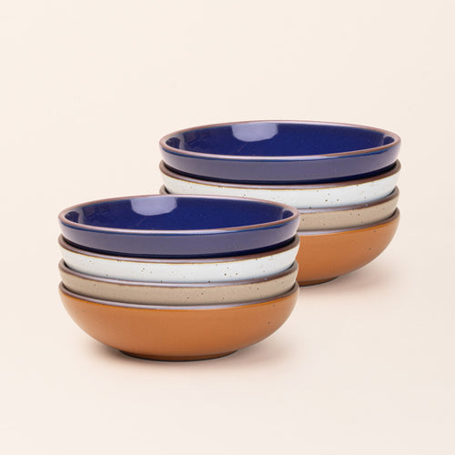 2 stacks of 4 dinner-sized shallow ceramic bowls in an earthy orange, glossy dark blue, white, and pale warm brown colors featuring iron speckles and an unglazed rim