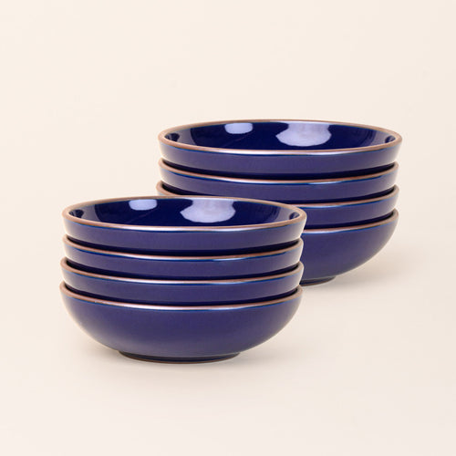 2 stacks of 4 dinner-sized shallow ceramic bowls in a glossy dark blue color featuring iron speckles and an unglazed rim