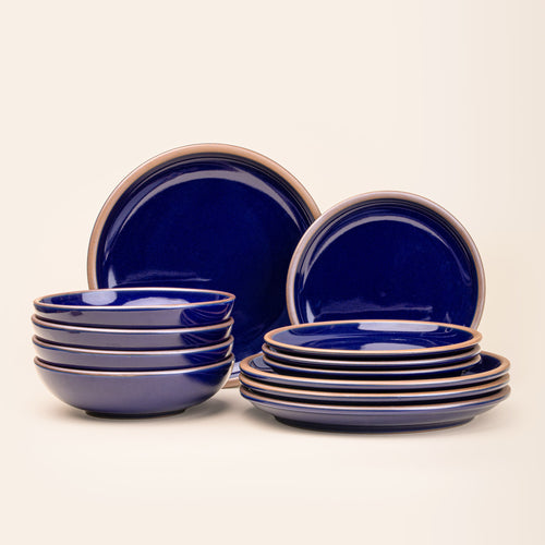 A set of stoneware dinnerware including four dinner plates, four side plates, and four bowls in a glossy dark blue color with iron speckles.