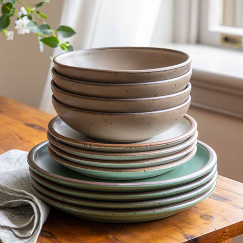 A 12-piece dinnerware set with four bowls, four dinner plates and four side plates in a viridian green, warm brown, warm white and cool white glazes.